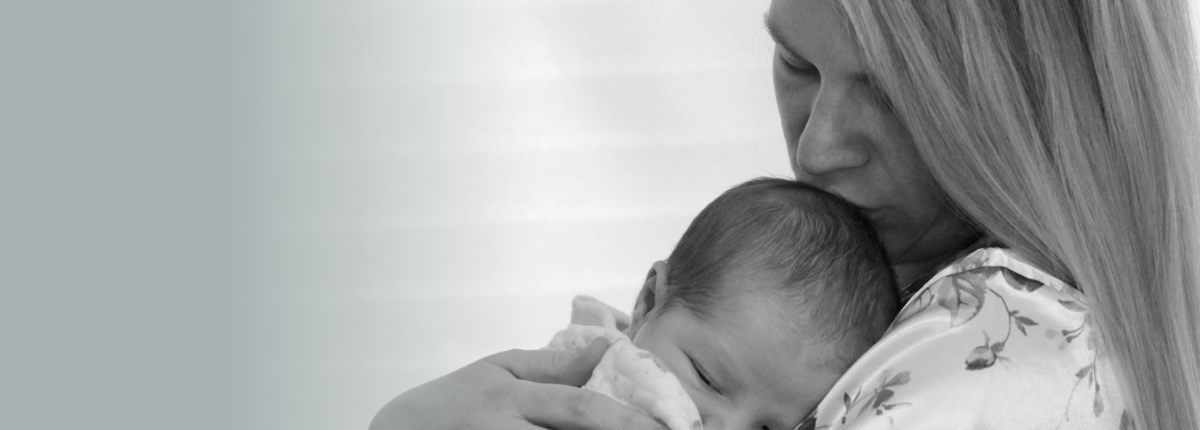 Woman holding a baby on her chest, kissing the baby's forehead.