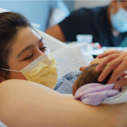 Mother just gave birth, with doctors placing the newborn on her chest. The mother looks ecstatic.