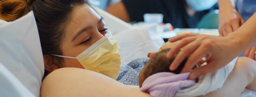 Mother just gave birth, with doctors placing the newborn on her chest. The mother looks ecstatic.