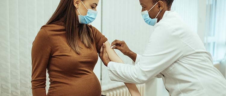 African American female doctor preparing a pregnant woman for a COVID-19 vaccination.