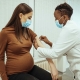 African American female doctor preparing a pregnant woman for a COVID-19 vaccination.